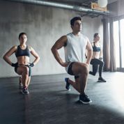 Zwei Frauen und ein Mann machen in einem Fitnessraum Kniebeugen Zwei Frauen und ein Mann machen in einem Fitnessraum Kniebeugen